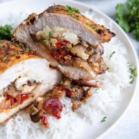 Stuffed chicken breast with mushrooms, sun dried tomatoes and cheese cut in half to show the filling, served over rice.