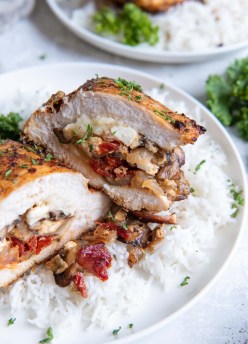 Stuffed chicken breast with mushrooms, sun dried tomatoes and cheese cut in half to show the filling, served over rice.