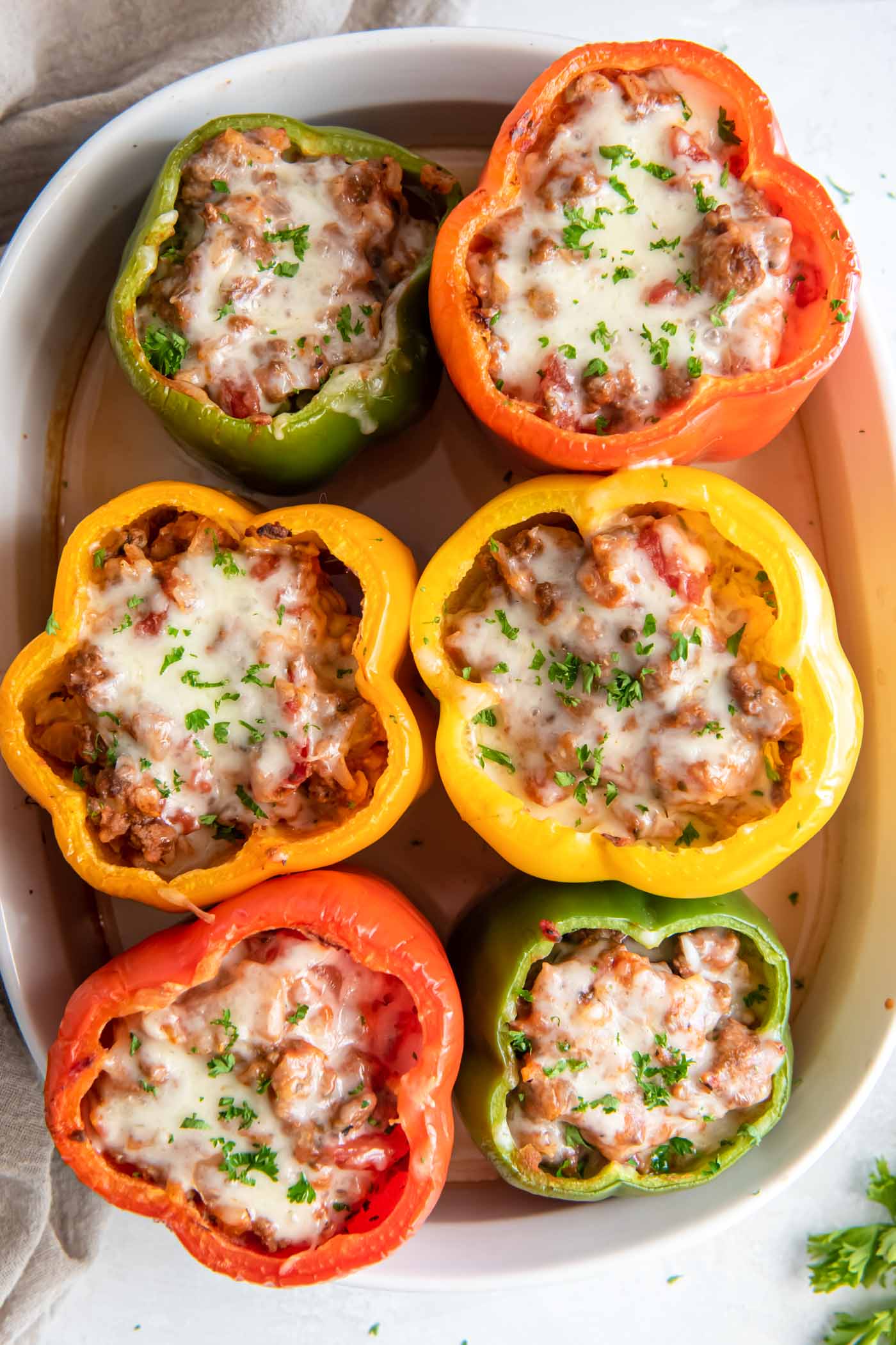 Six baked stuffed bell peppers in baking dish.