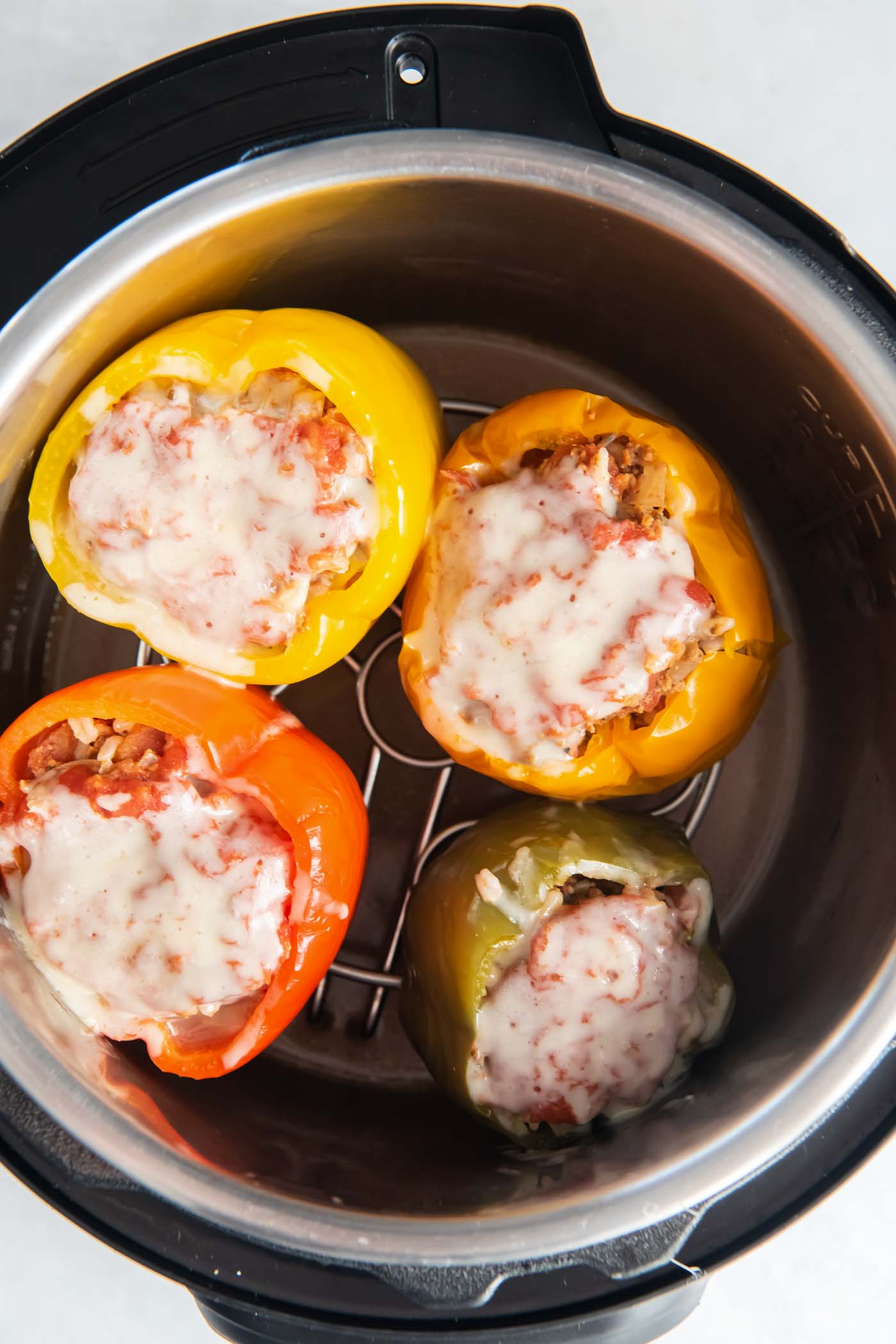 Four cooked stuffed peppers with cheese in instant pot.
