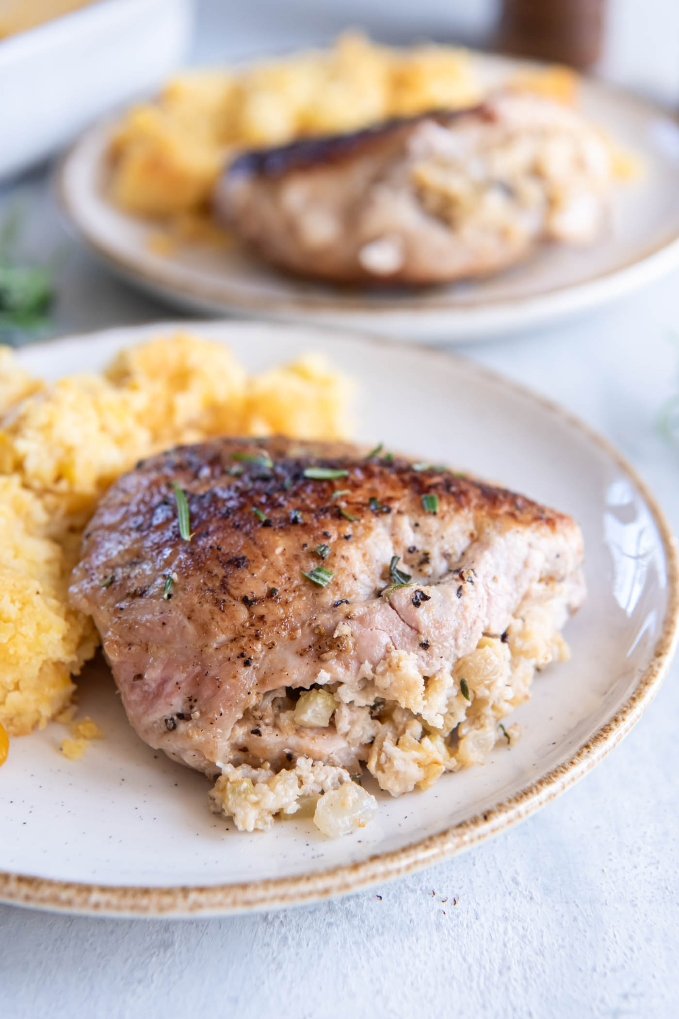 Pork chop stuffed with apple celery stuffing served on a plate with corn casserole.