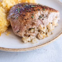 Baked boneless pork chop stuffed with apple stuffing served on a plate.