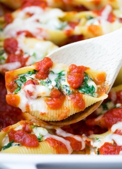 Stuffed pasta shell on serving spoon held over baking dish.