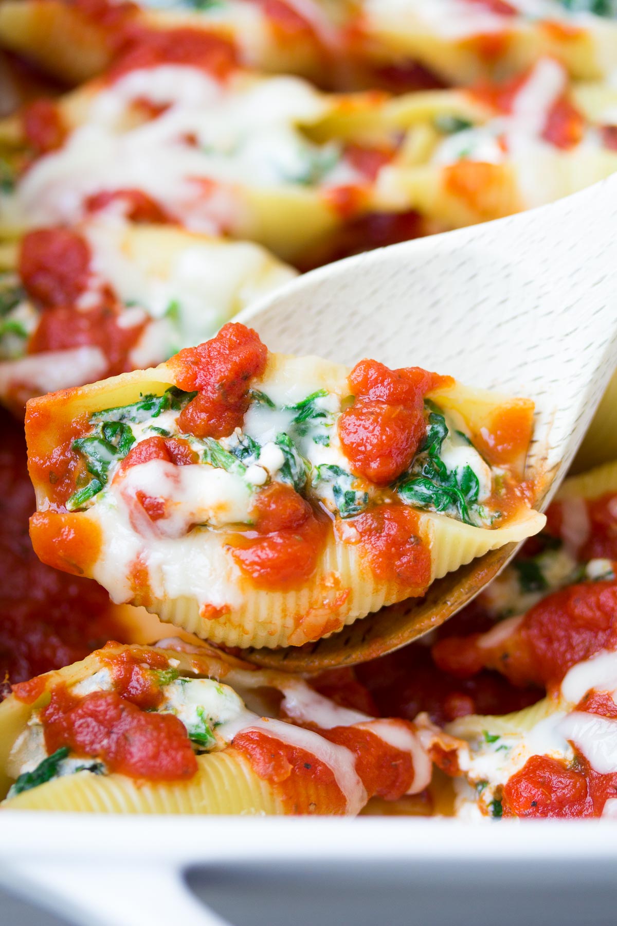 Stuffed pasta shell on serving spoon held over baking dish.