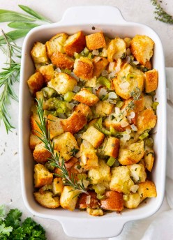 Homemade stuffing with fresh herbs in a white baking dish.