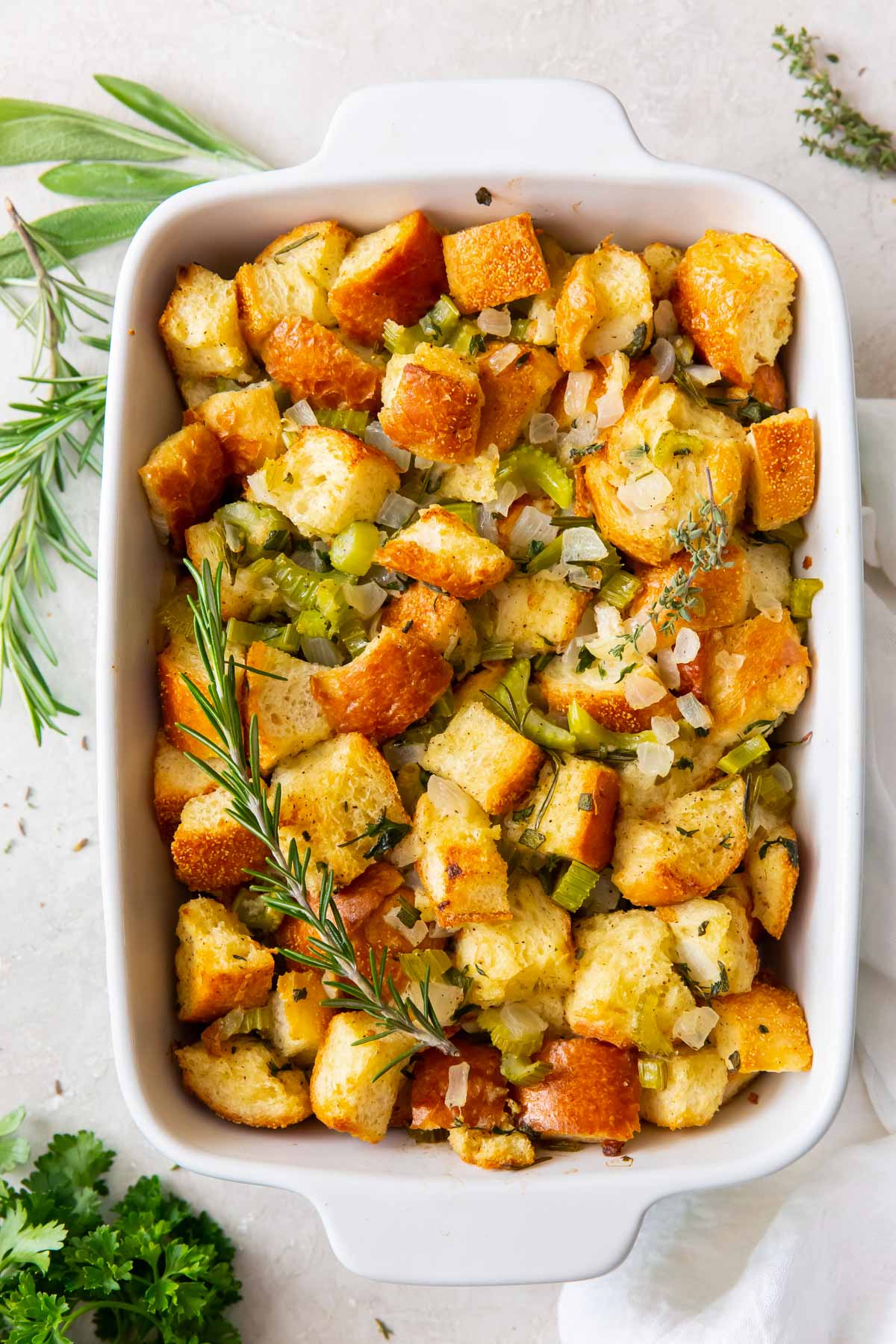 Thanksgiving stuffing with fresh herbs in a white baking dish.