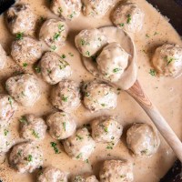 Swedish meatballs and sauce in a skillet with a wooden spoon.