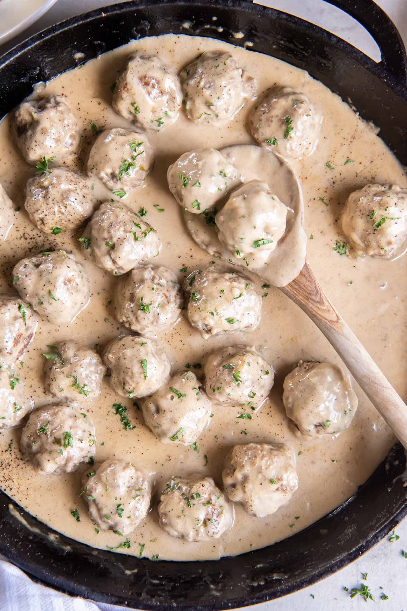 Swedish meatballs and sauce in a cast iron skillet with a wooden spoon.