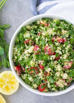 Tabouli salad served in a white bowl with lemons and parsley on the side.