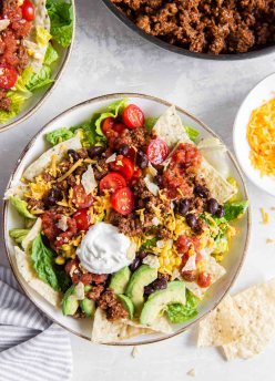 A serving of taco salad in a salad bowl with skillet of taco meat in the background.