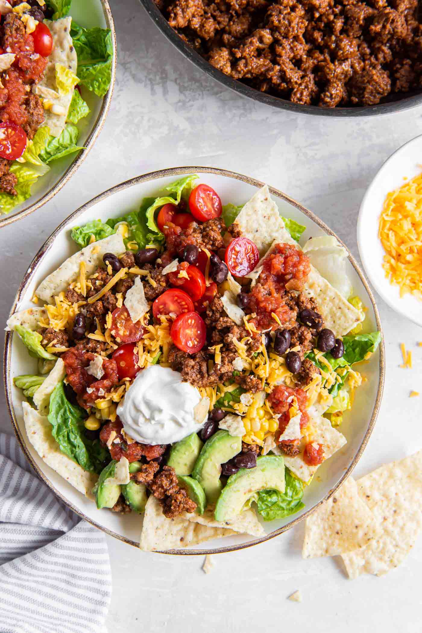 A serving of taco salad in a salad bowl with skillet of taco meat in the background.