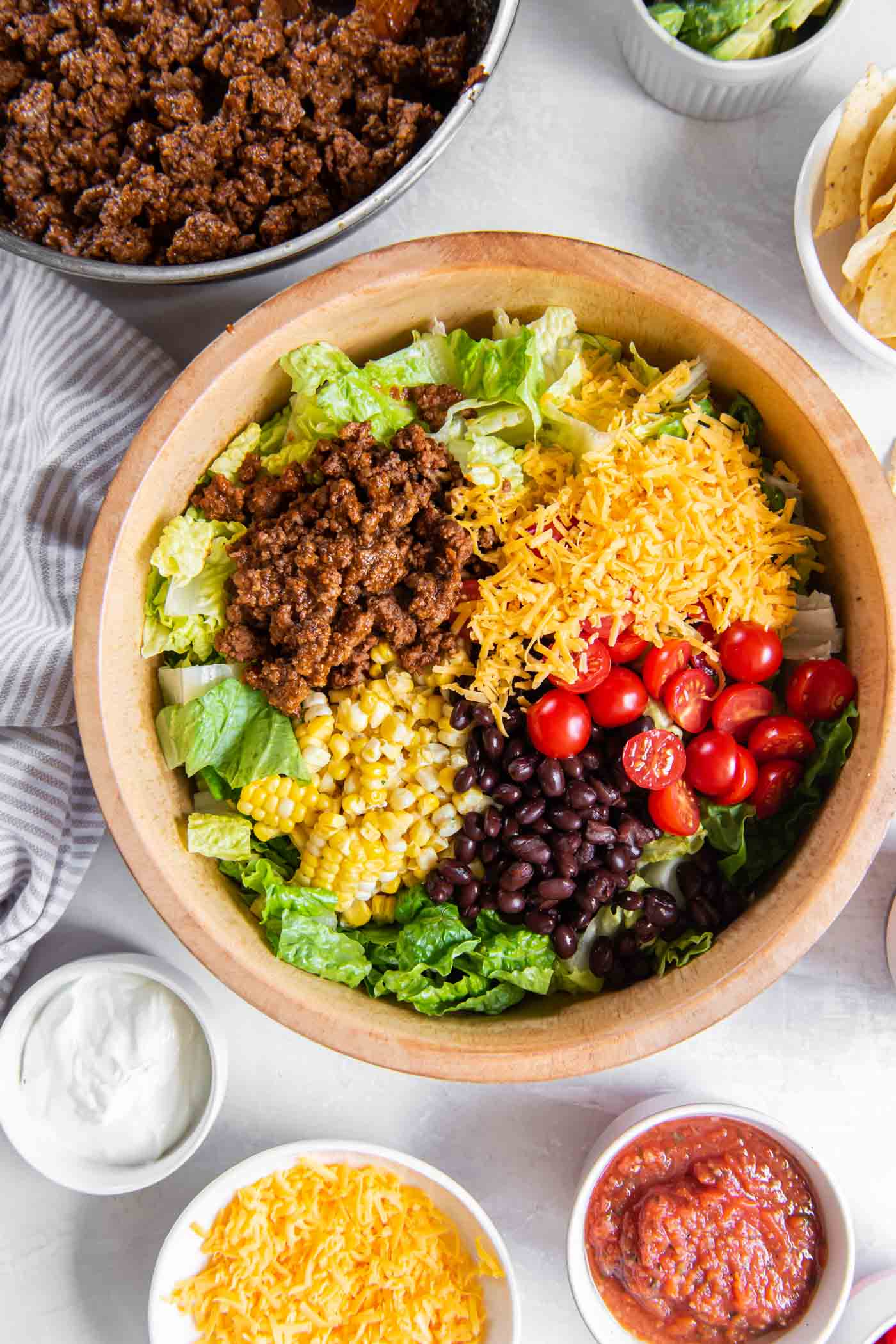 Taco salad ingredients added to a wooden serving bowl.