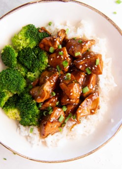 Teriyaki chicken plated with white rice, broccoli, sesame seeds and chopped green onions.
