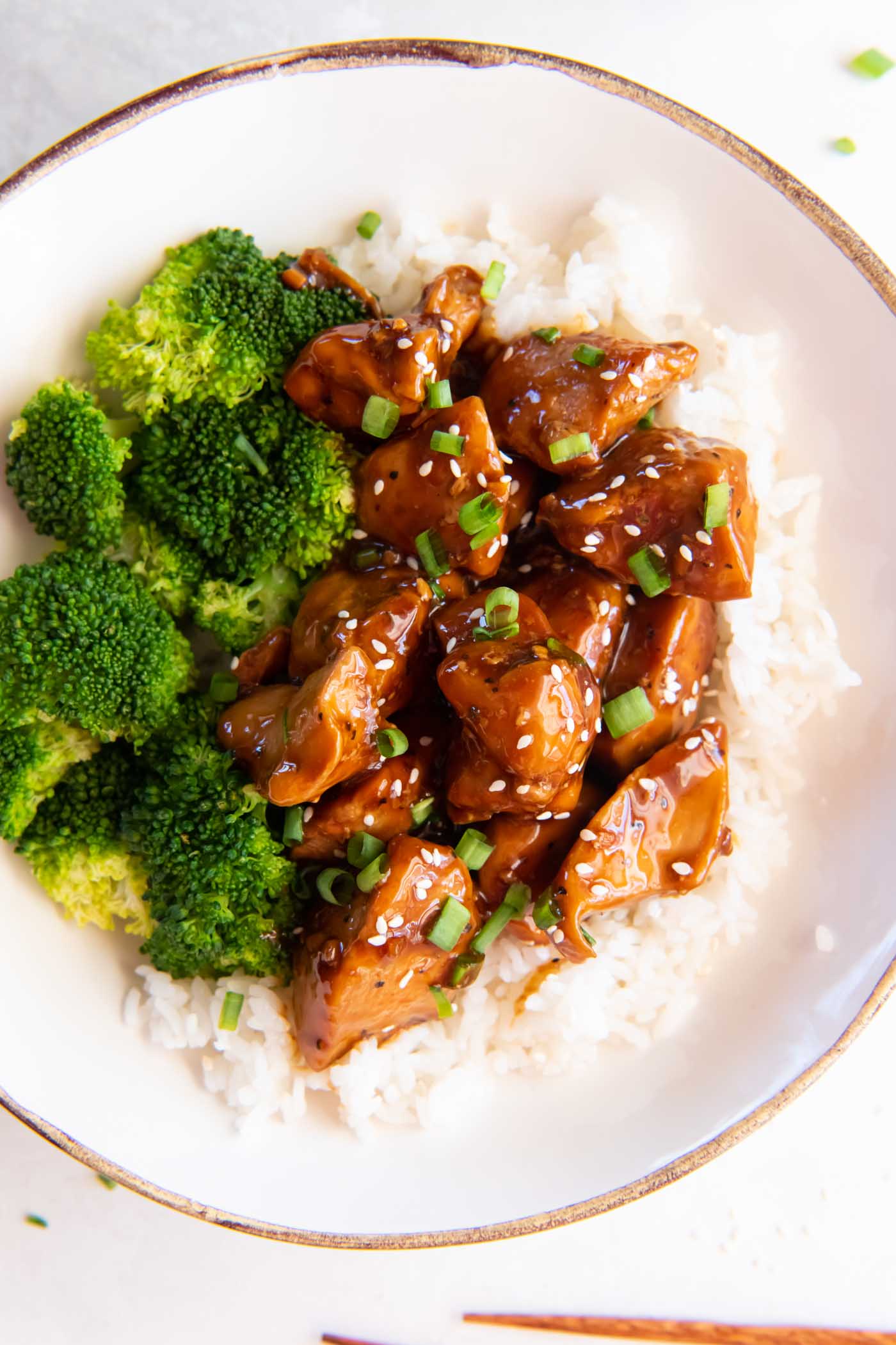 Teriyaki chicken plated with white rice, broccoli, sesame seeds and chopped green onions.