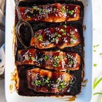 Baked teriyaki salmon in a baking dish with a spoon in the sauce.