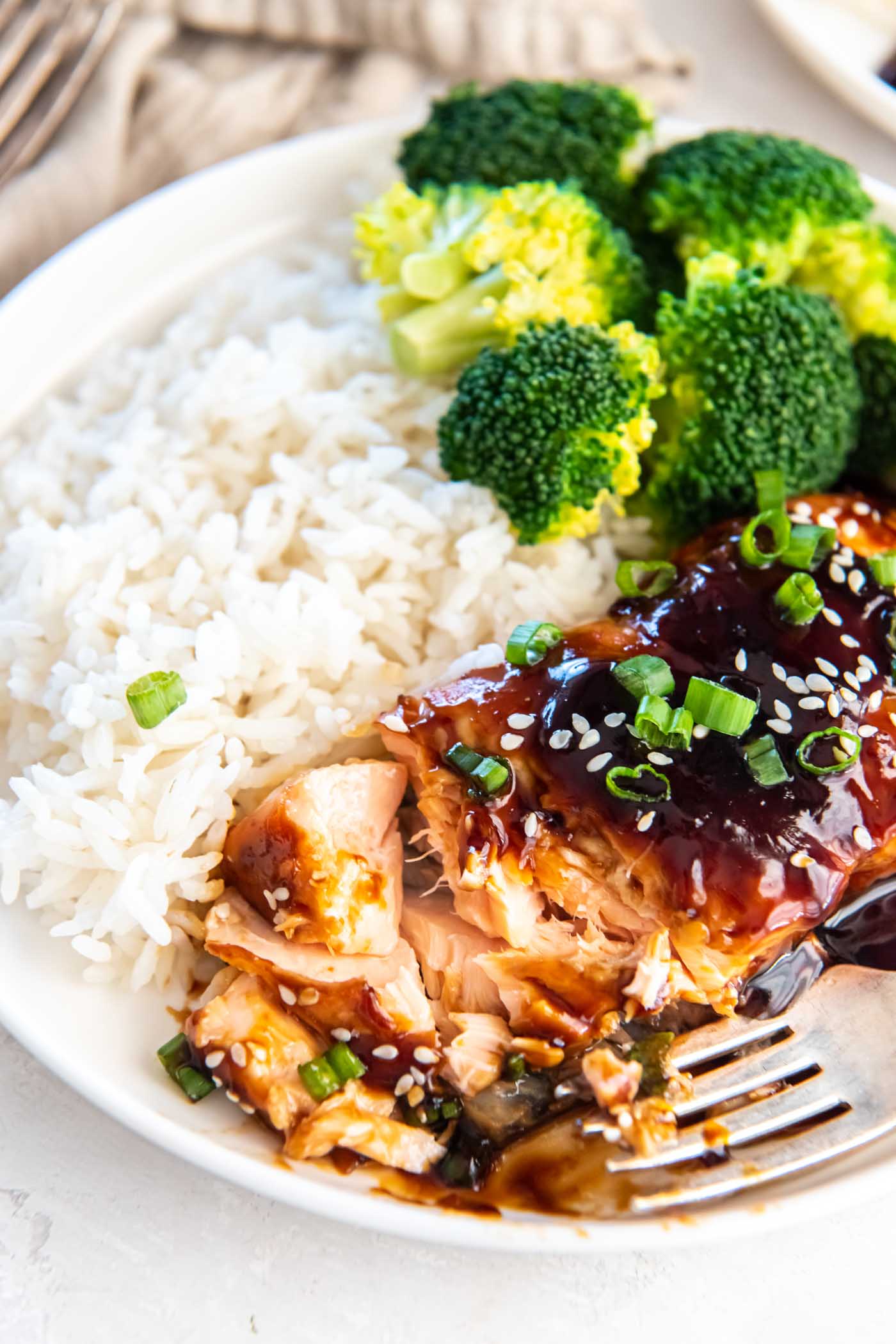 Fillet of teriyaki salmon partially flaked with a fork, served with white rice and broccoli.