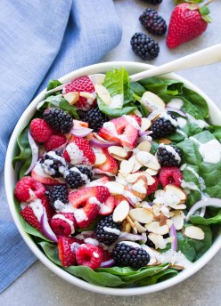 Berry spinach salad with poppy seed dressing drizzled over it.