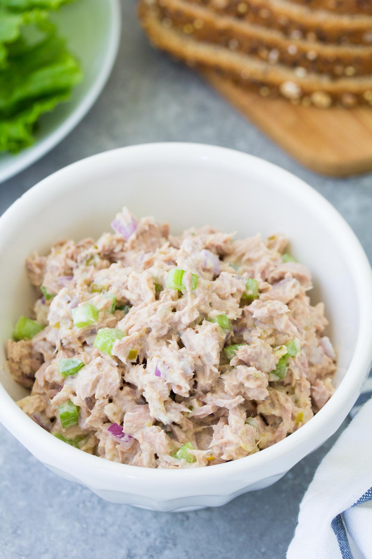 Tuna salad in a bowl with lettuce and bread slices in background.