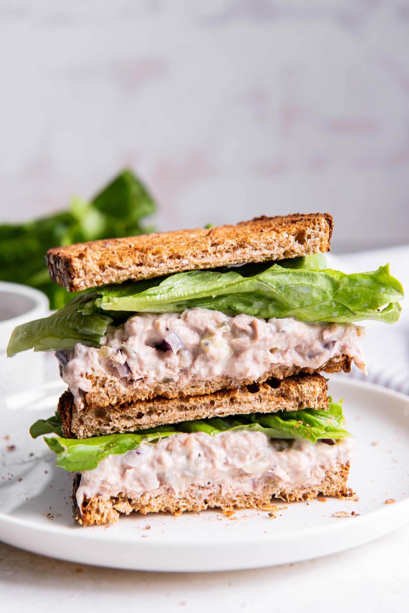 Two tuna salad sandwich halves with lettuce stacked on top of each other.