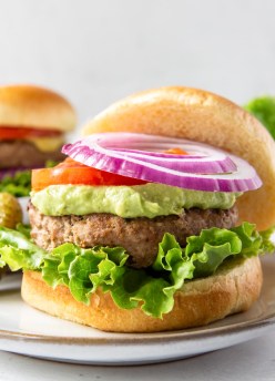 Turkey burger served on a bun with lettuce, guacamole, tomato and red onion.