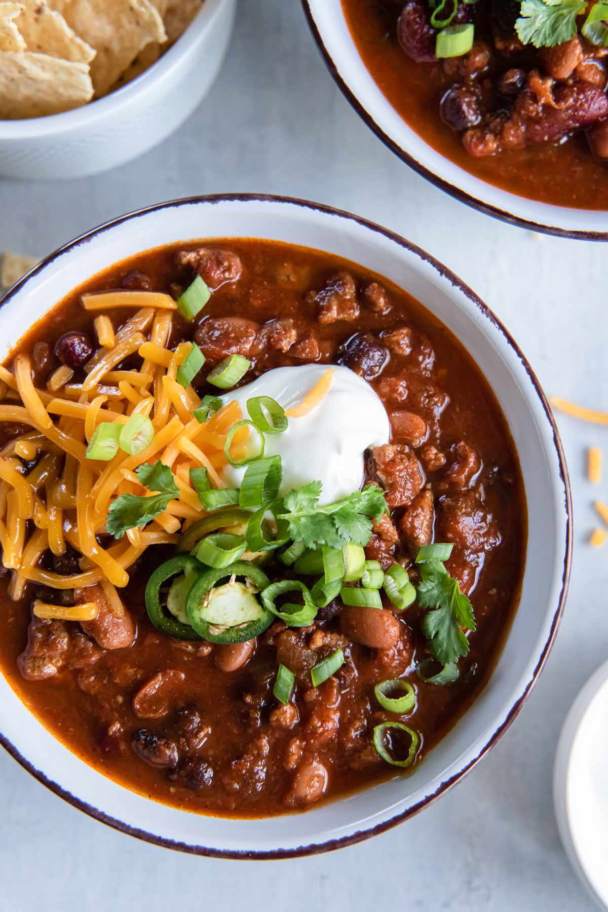 Turkey chili served in a bowl topped with sour cream, shredded cheddar, jalapenos, green onions and cilantro.
