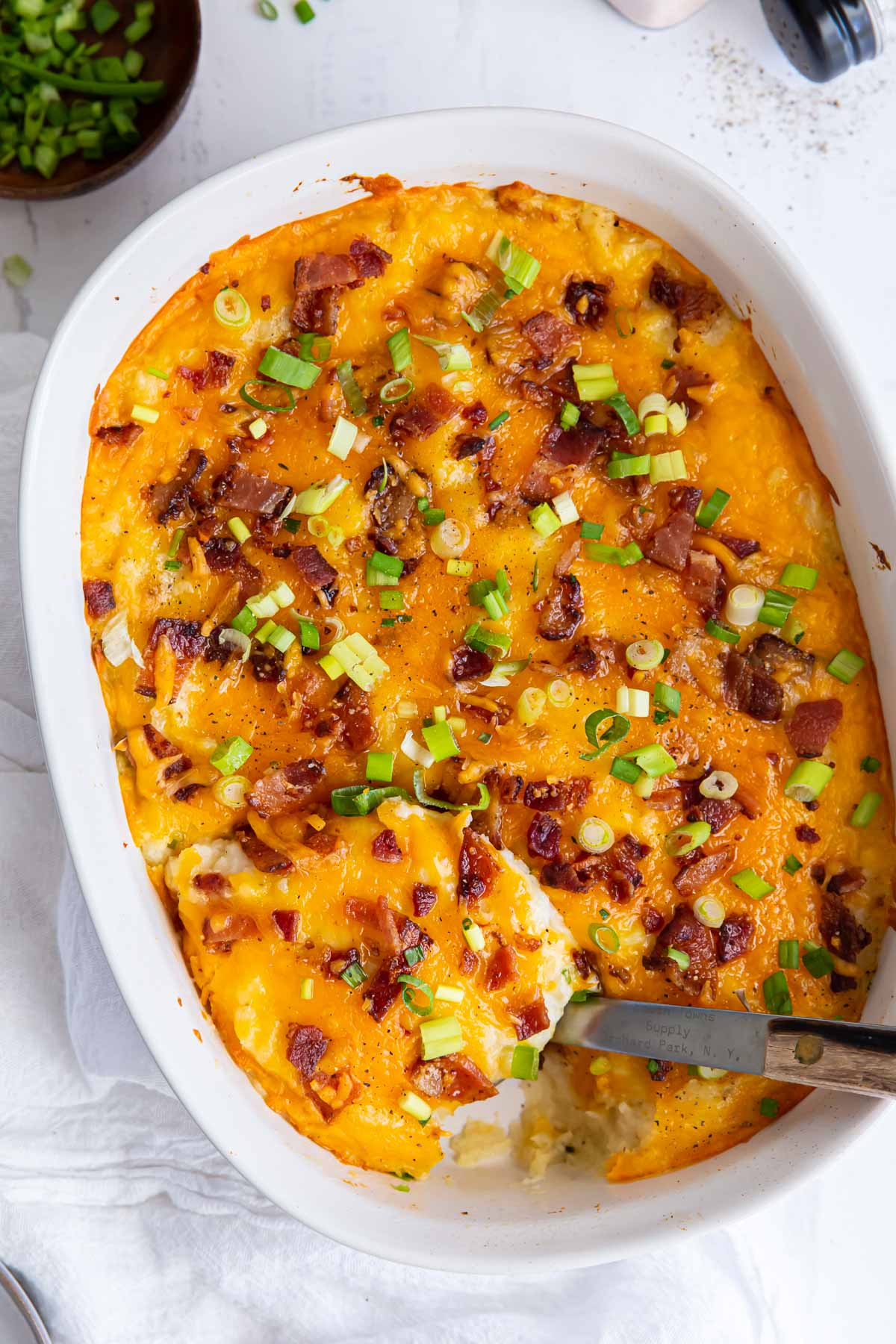 Twice baked potato casserole with bacon in casserole dish with a serving spoon.