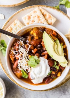 chili topped with sour cream, cheese and avocado with crackers on the side