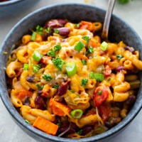 chili mac topped with cheese and green onions in a bowl with a spoon
