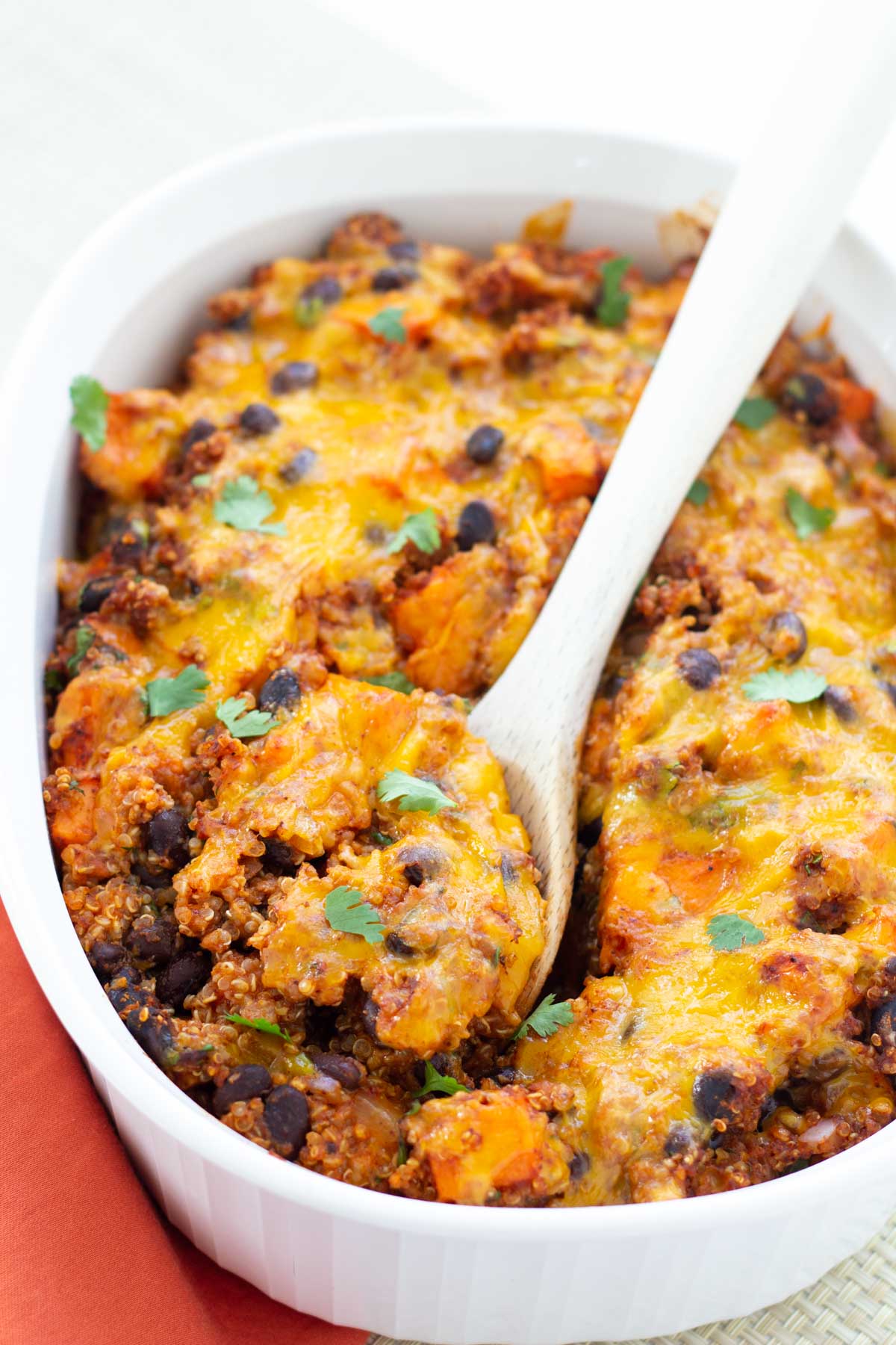 Vegetarian enchilada casserole in baking dish with wooden spoon.
